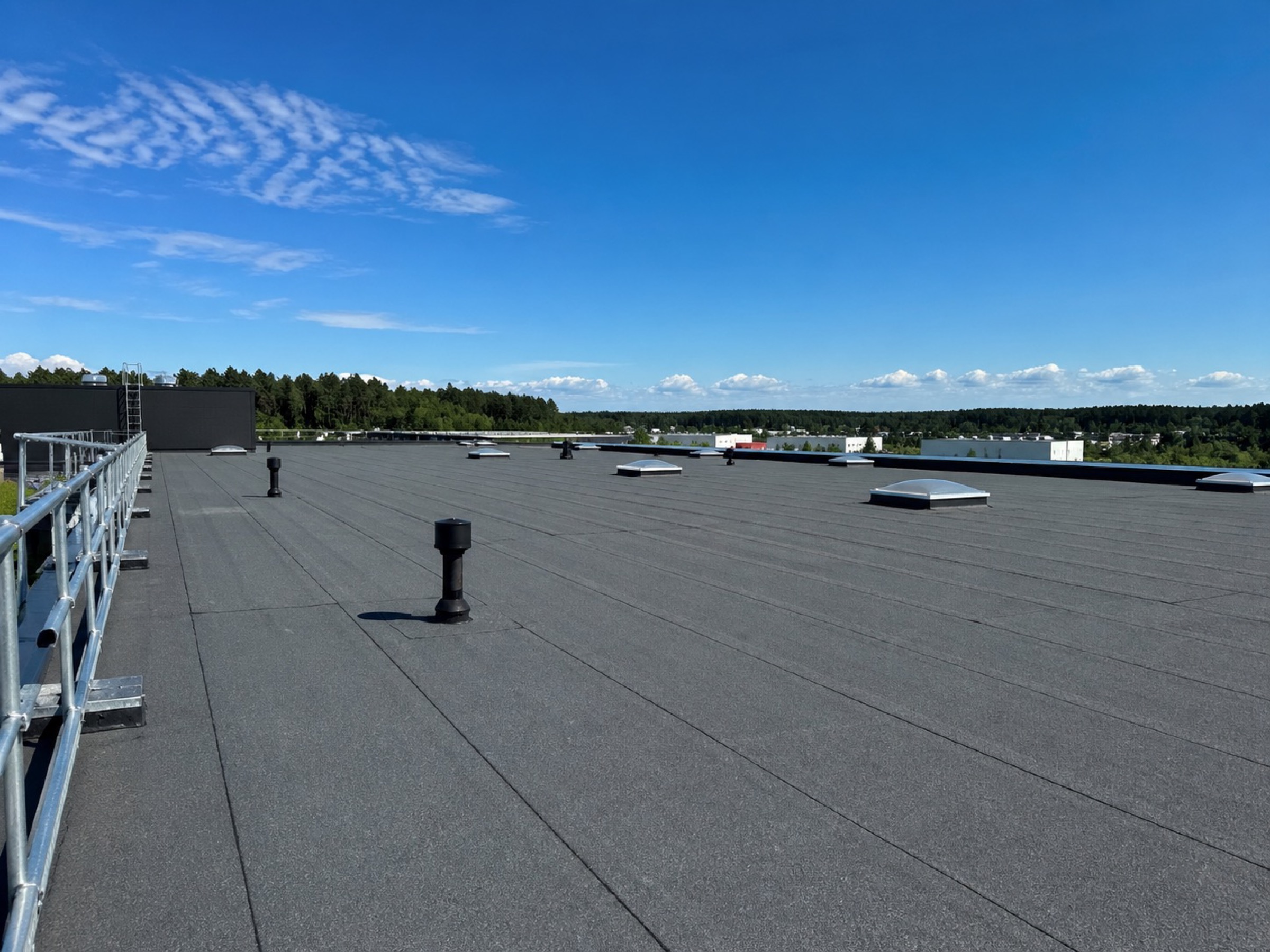 Industriellt papptak — stort flackt tak med skyltsfönster, ventilationsrör och fallskyddsräcke utfört av Arbetslag Bygg